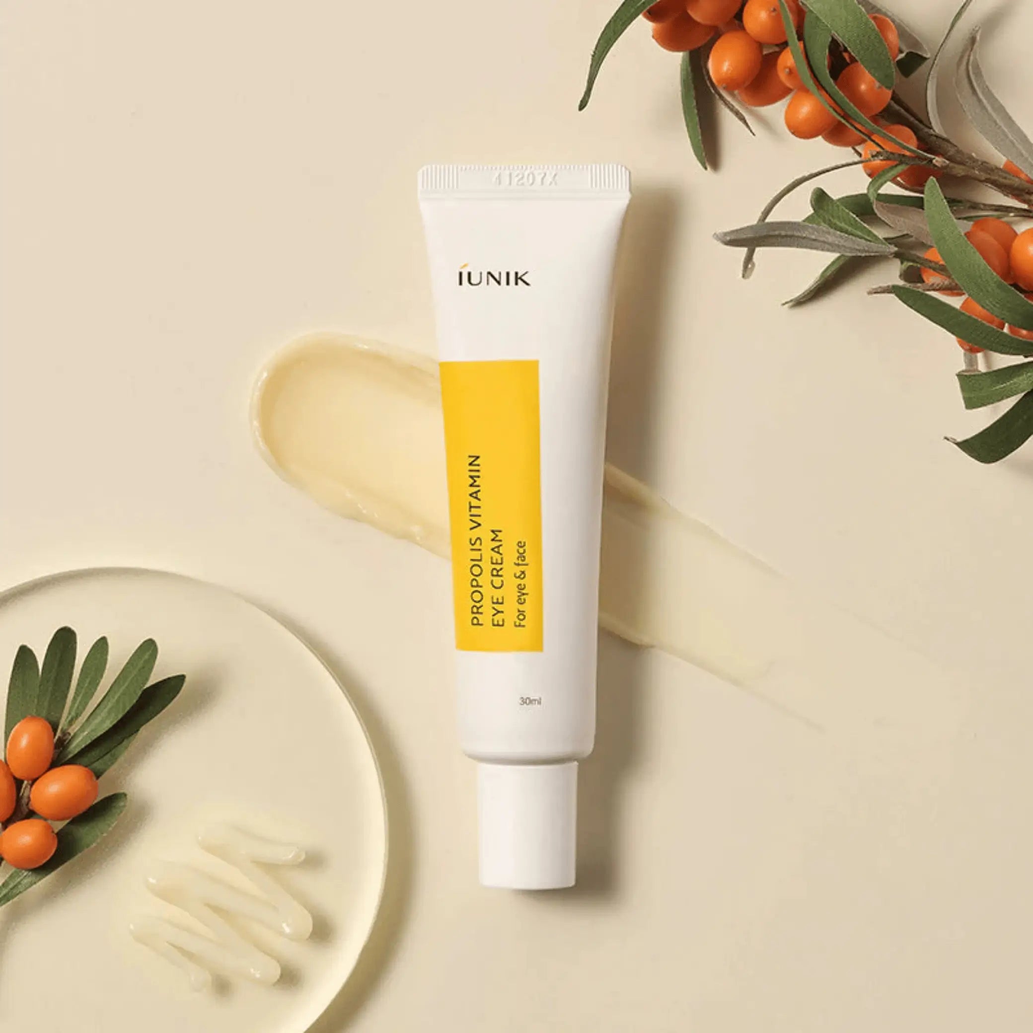 Propolis Vitamin Eye Cream da iUNIK tubo com prato e bagas laranja em fundo bege